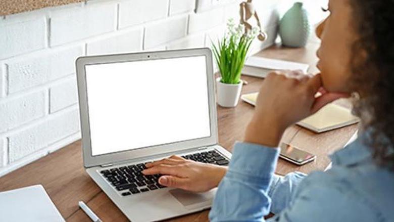 A female student wearing a blue shirt is pictured working at a laptop.